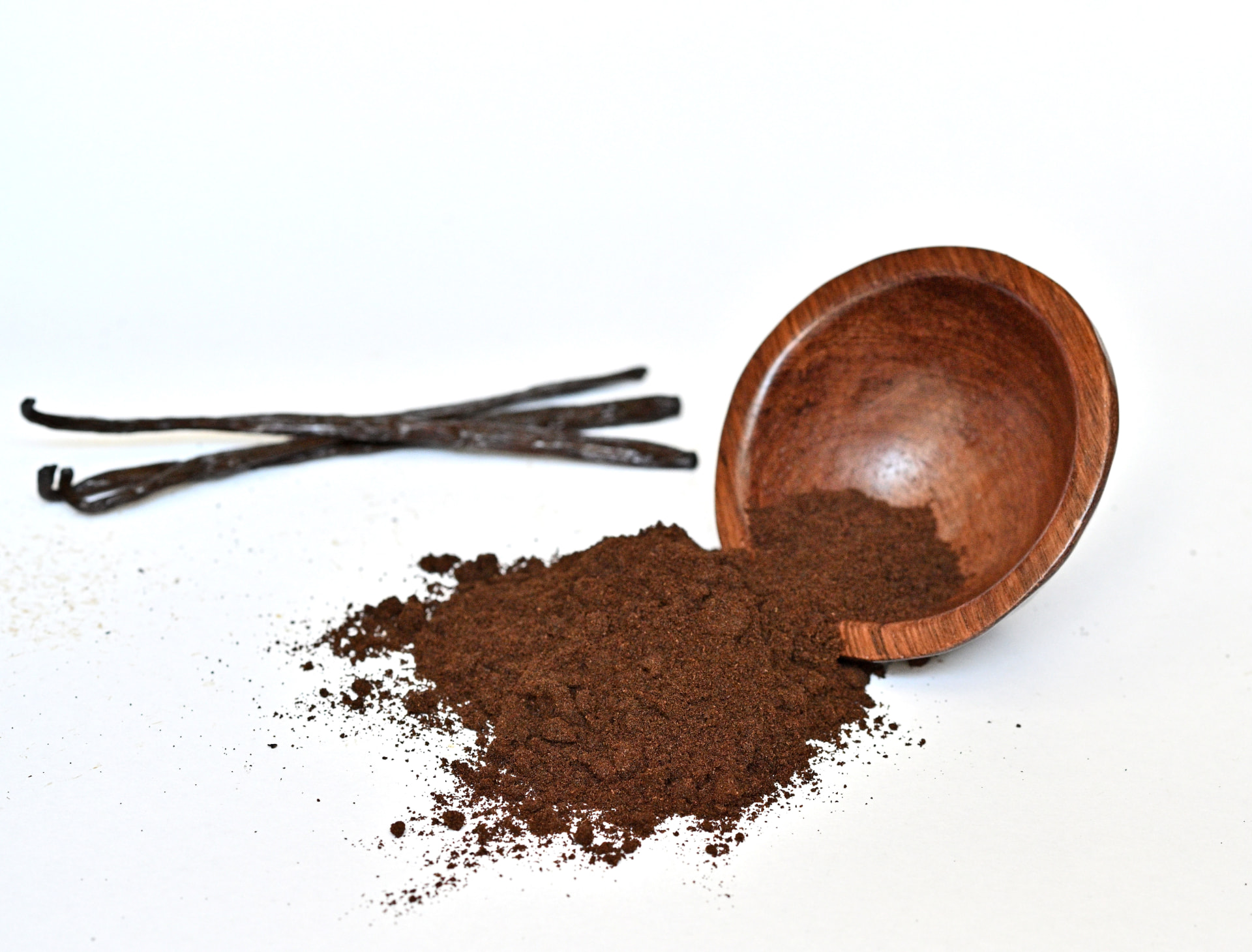 Wooden bowl of Madagascar vanilla powder with scattered powder and pods