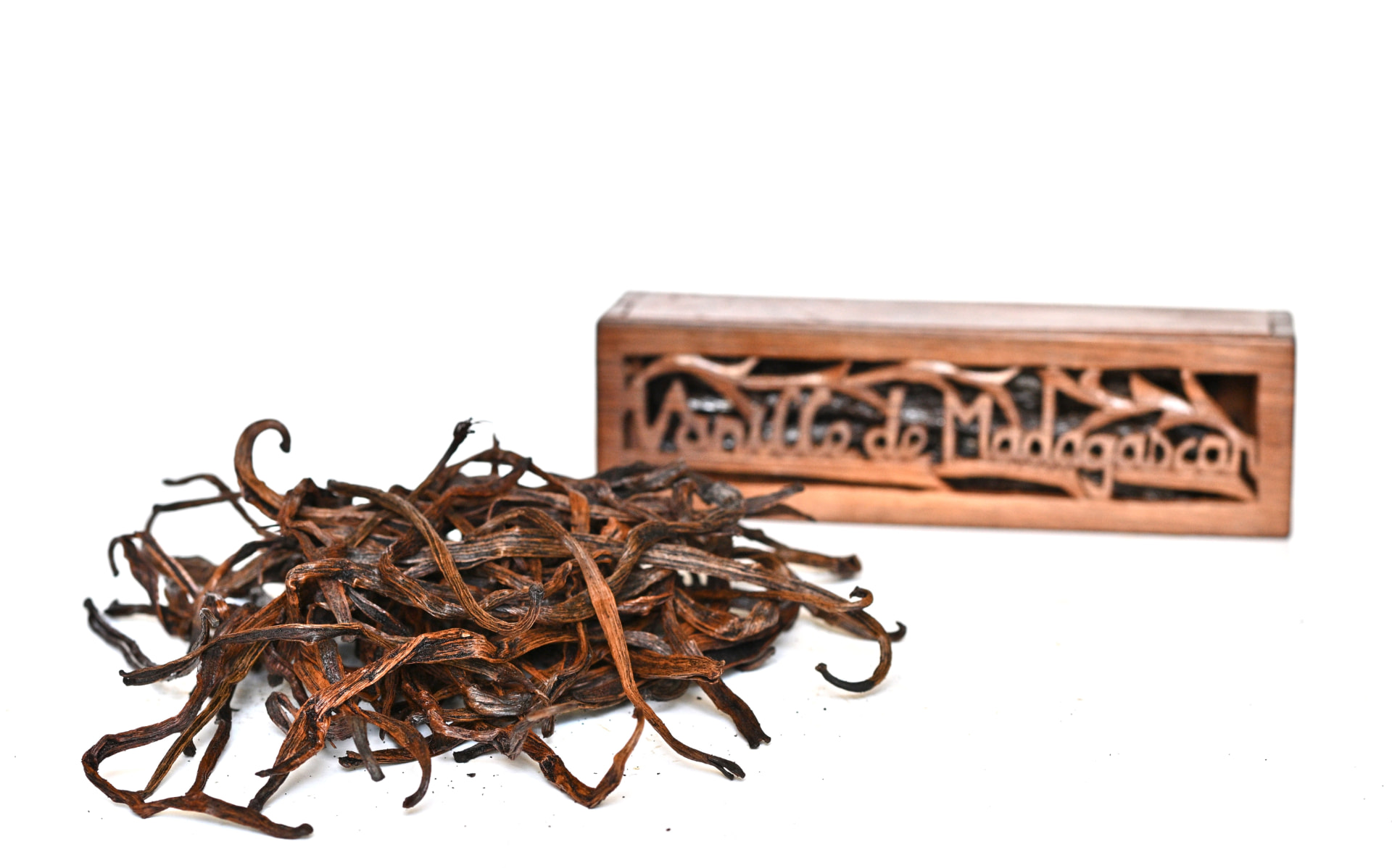 Pile of cut Madagascar vanilla beans beside a carved wooden box